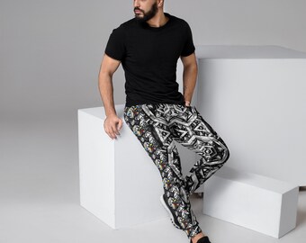 May include: Black t-shirt and patterned joggers. The joggers have a black and white geometric design with colourful accents. The person is wearing black trainers and is leaning against a white cube.