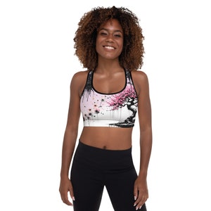 Puede incluir: Un sujetador deportivo blanco con un diseño de espalda de nadador negro y un estampado floral rosa y negro. El estampado presenta un árbol estilizado con flores rosas.
