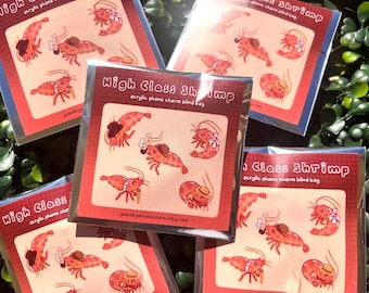 Könnte beinhalten: Ein Set mit sechs bunten Acryl-Handy-Anhängern mit Cartoon-Garnelen, die Hüte tragen und Accessoires halten. Die Anhänger sind in einer Blind Bag verpackt, d. h. der Käufer weiß nicht, welches Design er erhält. Die Anhänger sind mit "High Class Shrimp" beschriftet und auf Etsy erhältlich.