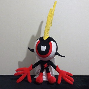 Puede incluir: Un juguete de peluche negro y rojo con un solo ojo grande y una cabeza en forma de rayo amarillo. El juguete tiene brazos y piernas rojos y está sentado sobre una superficie negra.