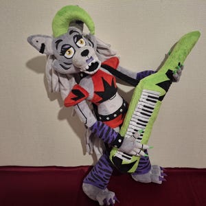 May include: A gray and white plush toy wolf with green hair and a red and black outfit is holding a green and white keyboard.