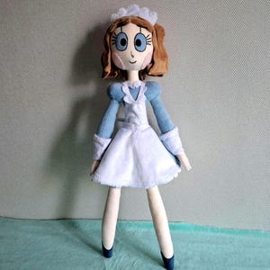 May include: A handmade doll dressed in a blue and white outfit, reminiscent of a maid's uniform. The doll has brown hair, blue eyes, and a sweet expression. The doll's legs are long and slender, and it wears blue shoes.