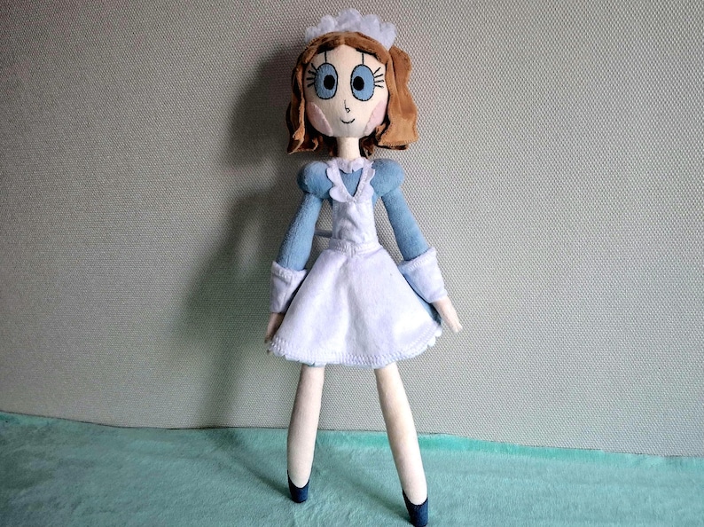 May include: A handmade doll dressed in a blue and white outfit, reminiscent of a maid's uniform. The doll has brown hair, blue eyes, and a sweet expression. The doll's legs are long and slender, and it wears blue shoes.