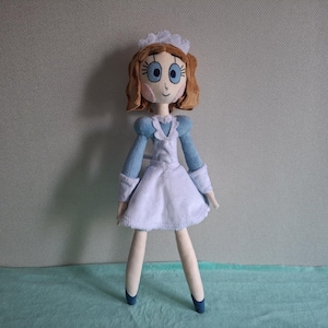 May include: A handmade doll dressed in a blue and white maid outfit. The doll has brown hair, blue eyes, and a white cap. The doll's legs and arms are a light beige color, and it is wearing blue shoes.