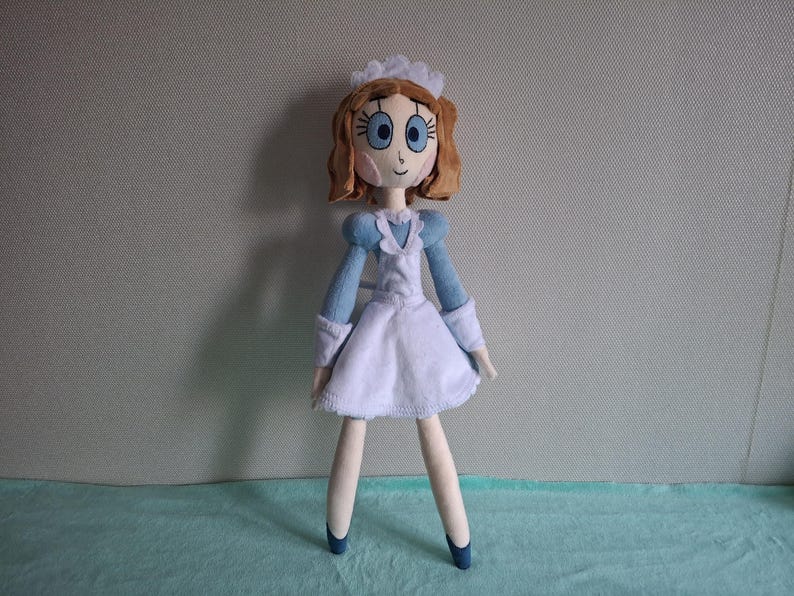 May include: A handmade doll dressed in a blue and white maid outfit. The doll has brown hair, blue eyes, and a white cap. The doll's legs and arms are a light beige color, and it is wearing blue shoes.