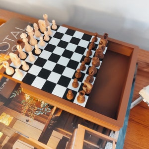 Op de afbeelding: Een bruin houten schaakbord met een zwart-wit geblokt speelveld. Het schaakbord is open en toont een spel in uitvoering met zowel witte als bruine schaakstukken.