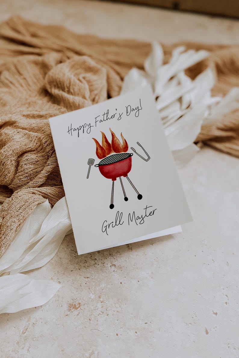 May include: A Father's Day card featuring a watercolour illustration of a red barbecue with flames, a spatula, and tongs. The card reads "Happy Father's Day!" and "Grill Master" in black script.