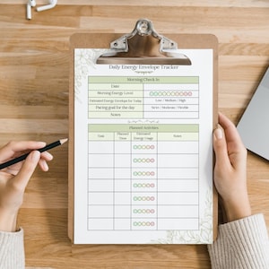 May include: A clipboard with a printed "Daily Energy Envelope Tracker" sheet. The sheet has sections for daily check-in and planned activities. A hand holds a pencil, ready to write. The clipboard is on a wooden surface.