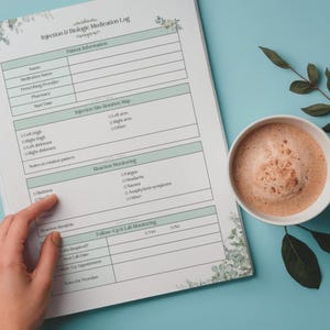May include: A medication log with a floral design, featuring sections for patient information, injection site rotation, and reaction monitoring. A cup of coffee sits beside the log on a light blue surface.