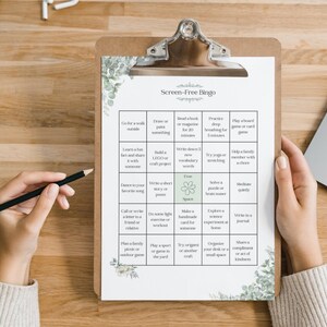 May include: A clipboard with a "Screen-Free Bingo" game sheet. The sheet has a grid of activities like "Go for a walk outside" and "Write in a journal." The clipboard is held by a person with a pencil.