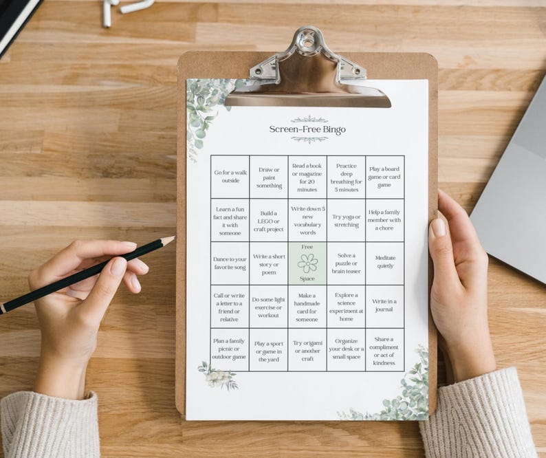 May include: A clipboard with a "Screen-Free Bingo" game sheet. The sheet has a grid of activities like "Go for a walk outside" and "Write in a journal." The clipboard is held by a person with a pencil.