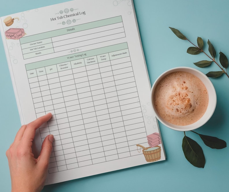 Peut inclure: Un cahier "Hot Tub Chemical Log" avec un design vert clair et blanc. Le cahier est ouvert, avec une main pointant vers la section "Water Testing Log". Une tasse de caf&eacute; et une branche de feuilles sont sur une surface bleu clair.