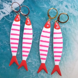 Può includere: Quattro paia di orecchini a forma di pesce. Ogni orecchino è bianco con strisce orizzontali rosa, una coda rossa e una testa rossa con un piccolo punto nero. Due paia hanno ganci per le orecchie color argento e due paia hanno ganci per le orecchie color oro.
