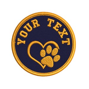 Pode incluir: Um remendo redondo bordado de cor azul marinho com um contorno dourado. O remendo apresenta uma pegada dourada dentro de um coração dourado com o texto "YOUR TEXT" ao redor.