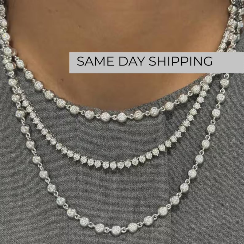 May include: A layered necklace set consisting of three silver-toned chains, each featuring a continuous row of round, clear, faceted stones set in metal bezels. The design creates a cascading effect around the neck, with each chain varying in length.