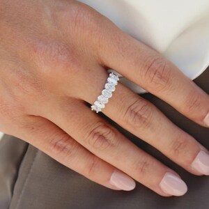 Pu&ograve; includere: Primo piano di un anello con pi&ugrave; diamanti taglio ovale disposti in fila. L'anello &egrave; al dito di una persona, con la mano e parte del braccio visibili. L'anello &egrave; ambientato su uno sfondo neutro.