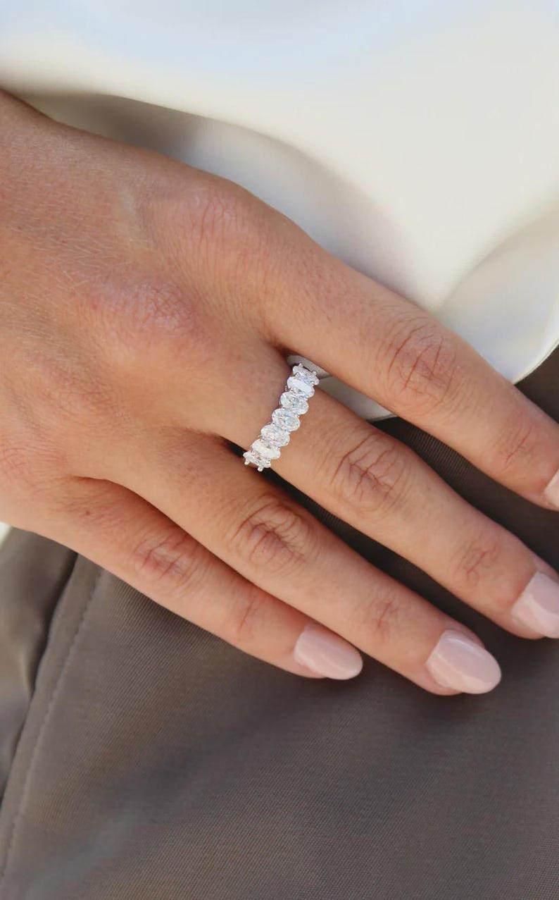 Pu&ograve; includere: Primo piano di un anello con pi&ugrave; diamanti taglio ovale disposti in fila. L'anello &egrave; al dito di una persona, con la mano e parte del braccio visibili. L'anello &egrave; ambientato su uno sfondo neutro.