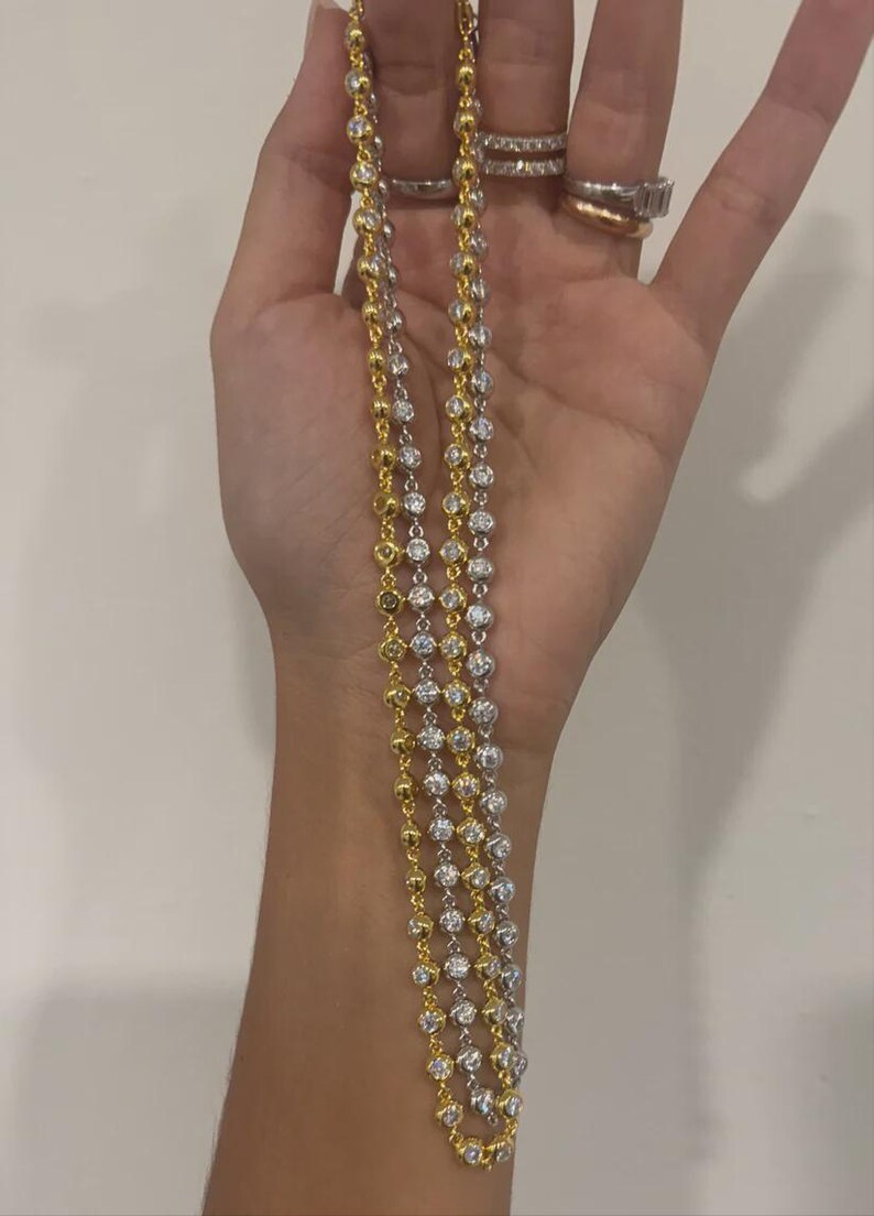 May include: A layered necklace set consisting of one gold-tone chain and one silver-tone chain, both featuring a continuous series of round, clear, faceted stones set in individual metal bezels that create a sparkling, uniform appearance.