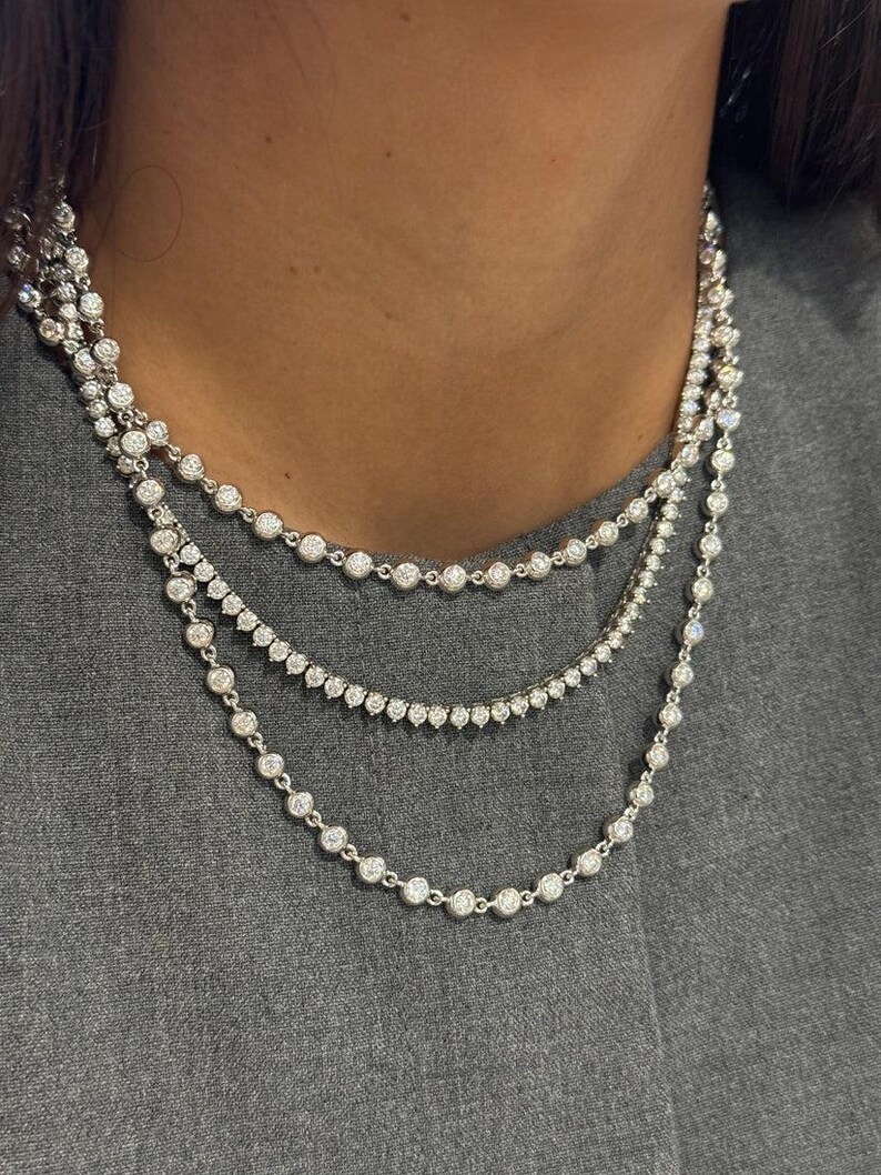 May include: A layered necklace set consisting of three separate silver-toned chains. Each chain features a series of small, round, clear stones set in individual metal bezels, creating a continuous sparkling effect around the neck.