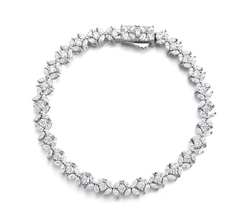 May include: A silver bracelet with a floral design. The bracelet features multiple clear, sparkling stones set in a delicate pattern. The clasp is rectangular and also set with stones. The bracelet is displayed on a white background.