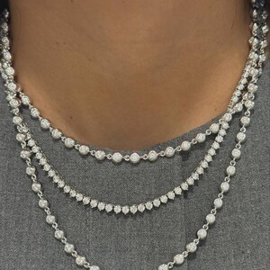 May include: A layered necklace set consisting of three separate silver-toned chains. Each chain features a series of round, clear, sparkling stones set in individual metal bezels, creating a continuous, uniform, and reflective design around the neck.