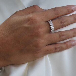 Pu&ograve; includere: Un anello d'argento con pi&ugrave; pietre ovali &egrave; mostrato su una mano. Le pietre dell'anello sono disposte in fila. Lo sfondo &egrave; un tessuto bianco.
