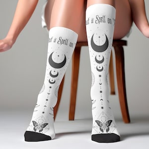 May include: White knee-high socks with a black and white design featuring a crescent moon, stars, and a butterfly. The socks have the text "Put a Spell on You" printed on them.