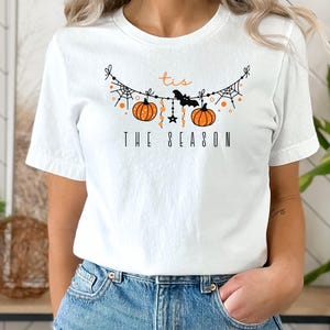 May include: White t-shirt with a black and orange graphic of a pumpkin garland with the text "Tis the Season".