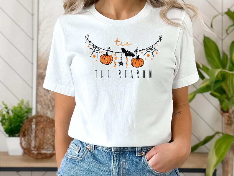 May include: White t-shirt with a black and orange graphic of a pumpkin garland with the text "Tis the Season".