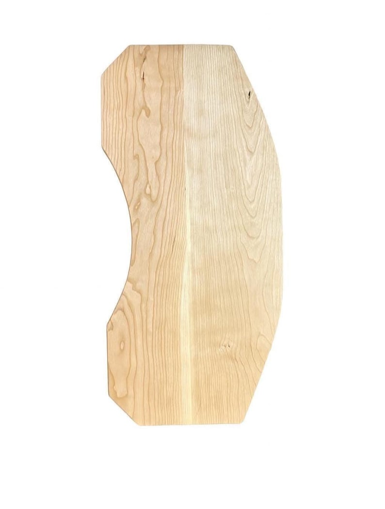 May include: A light-colored, wooden cutting board with a unique, curved design. The board has a natural wood grain pattern and a smooth surface. The shape is asymmetrical, with one side featuring a curved edge and the other side having a straight edge.