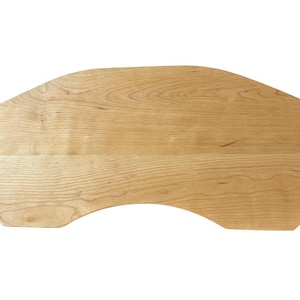 May include: A light-colored wooden desk top with a unique shape. The desk top has a curved front edge and a rectangular back. The wood grain is visible, and the color is a light tan.