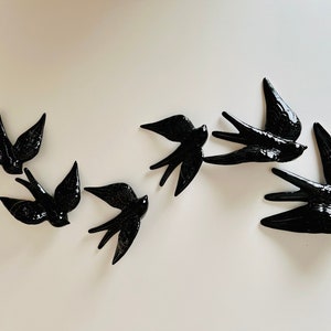 May include: Seven glossy black swallow figurines are displayed on a white surface. The birds are shown in flight, with detailed wings and feather patterns. These decorative swallows are ideal for adding a touch of nature-inspired elegance to any room or space.