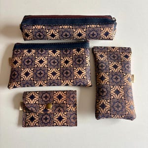 May include: A set of four cork accessories featuring a dark blue and tan geometric tile pattern. The collection includes a rectangular pencil case with a zipper, a flat zippered pouch, a small envelope-style wallet with a snap, and a tall slim case.