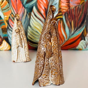Może przedstawiać: Dwie ceramiczne figurki przedstawiające osoby stojące obok siebie. Figurka po lewej stronie jest biała z fakturowaną powierzchnią. Figurka po prawej stronie jest brązowa z fakturowaną powierzchnią.