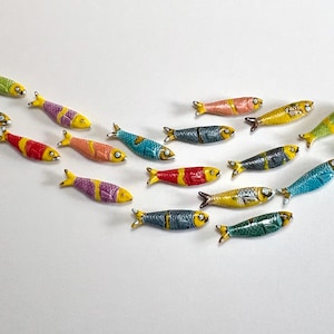 Puede incluir: Un conjunto de figuras decorativas de peces de colores dispuestas en forma curva. Los peces están pintados en varios colores, incluyendo amarillo, verde, rojo y azul, con detalles a rayas y estampados. Parecen ser de cerámica o metal pintado.