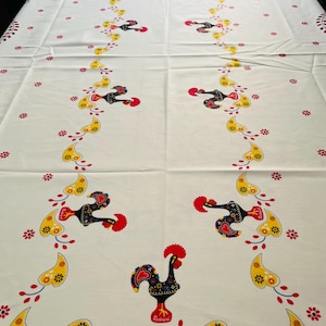 May include: White tablecloth with a repeating pattern of red, yellow and black roosters with blue accents. The roosters are surrounded by yellow and red stylised leaves. The tablecloth has the word "Portugal" printed on it.