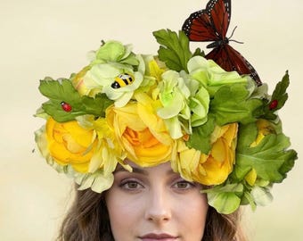 May include: A floral crown featuring yellow and green flowers, green leaves, and a large brown butterfly. The crown also includes a small ladybug and a bee. The crown is worn on a person's head.