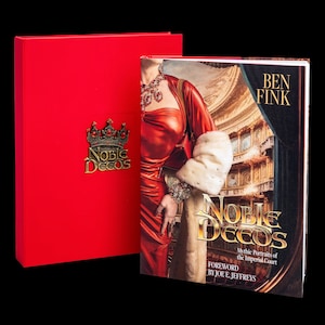 May include: A red hardcover book titled "Noble Decos: Mythic Portraits of the Imperial Court" by Ben Fink with a foreword by Joe E. Jeffreys. The book cover features a woman in a red dress and a white fur stole.