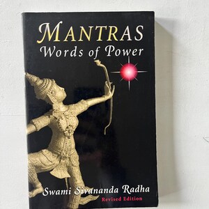 May include: A book titled "Mantras Words of Power" with a black cover. The cover features gold lettering and an illustration of a figure with a bow and arrow. The author's name, Swami Sivananda Radha, is also printed on the cover.