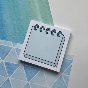 May include: A light blue notepad with a spiral binding. The notepad is on a blue and white watercolor background.