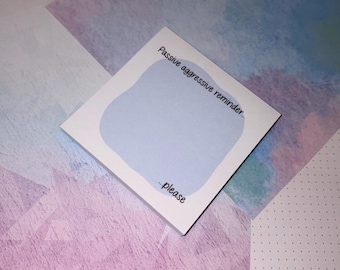 May include: A white sticky note with the text "Passive aggressive reminder... ...please" in black. The note has a light blue blob in the center. The background is a mix of pink, blue, and white geometric shapes.