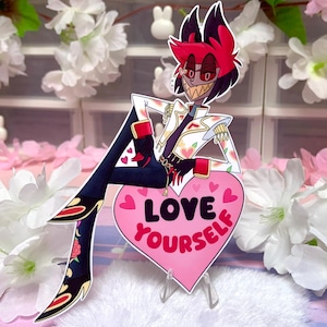 May include: A cartoon character with red hair and a white jacket, sitting on a pink heart-shaped sign that reads "LOVE YOURSELF". The character is wearing black trousers and boots with floral designs. The background includes pink and white flowers.