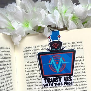 Könnte beinhalten: Ein blaues und rotes Lesezeichen mit einem Cartoon-Fernseher und dem Text "Trust Us With This Page".