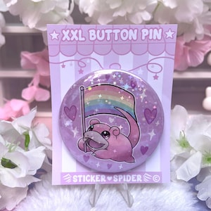 May include: A large, round button pin with a pink Slowpoke character holding a rainbow flag. The pin is on a light purple backing with the text "XXL BUTTON PIN" and "STICKER SPIDER". Hearts and stars decorate the background.