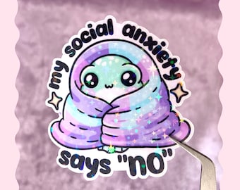 Puede incluir: Una pegatina con una criatura de dibujos animados envuelta en una manta con un patrón de arcoíris y purpurina. El texto dice "my social anxiety says 'no'".