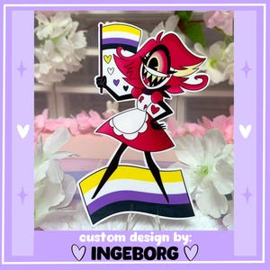 Op de afbeelding: Een sticker met een cartoonfiguur in een rode jurk, die een non-binaire pride-vlag vasthoudt. Het personage heeft rood haar en een brede grijns. De sticker staat tegen een bloemenachtergrond, met de tekst "custom design by: INGEBORG".