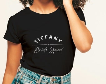 Może przedstawiać: Czarny T-shirt z białym tekstem, który brzmi "Tiffany Bride Squad".