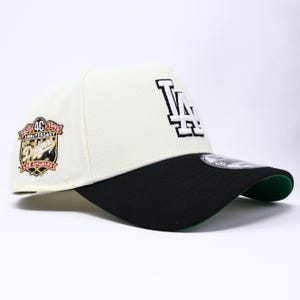 May include: Cream-colored baseball cap with a black brim and green underside. Features the Los Angeles Dodgers logo in white and a 40th Anniversary patch. A stylish accessory for sports fans.
