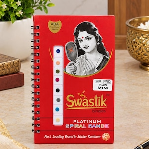 May include: A red spiral-bound booklet of Swastik brand mini bindis featuring a black and white illustration of a person holding a mirror. The cover displays the text 960 BINDI PLAIN MINI, PLATINUM SPIRAL RANGE, and No.1 Leading Brand in Sticker Kumkum.