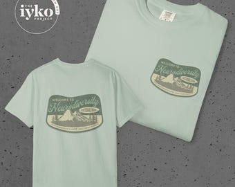 May include: Two light green t-shirts with a graphic that reads "Welcome to Neurodiversity National Park." The graphic features a mountain range and trees. The shirts have the text "The iYKO Project" in a circle at the top left.